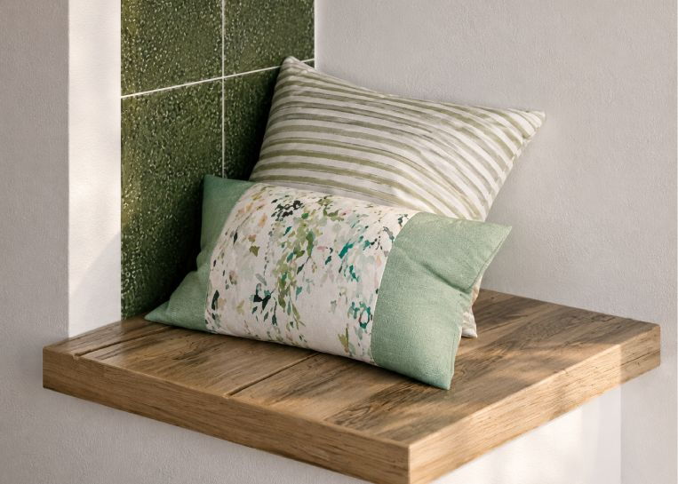 Nahaufnahme einer rustikalen Holz-Sitzbank am Ofen mit hellgrünen Kissen vor einer grünen Keramikwand.