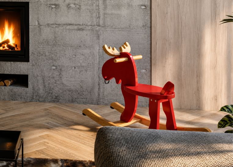 Detaillierte Ansicht eines klassischen roten Schaukelpferds aus Holz, das als farbiger Akzent vor der grauen Wandgestaltung platziert wurde.