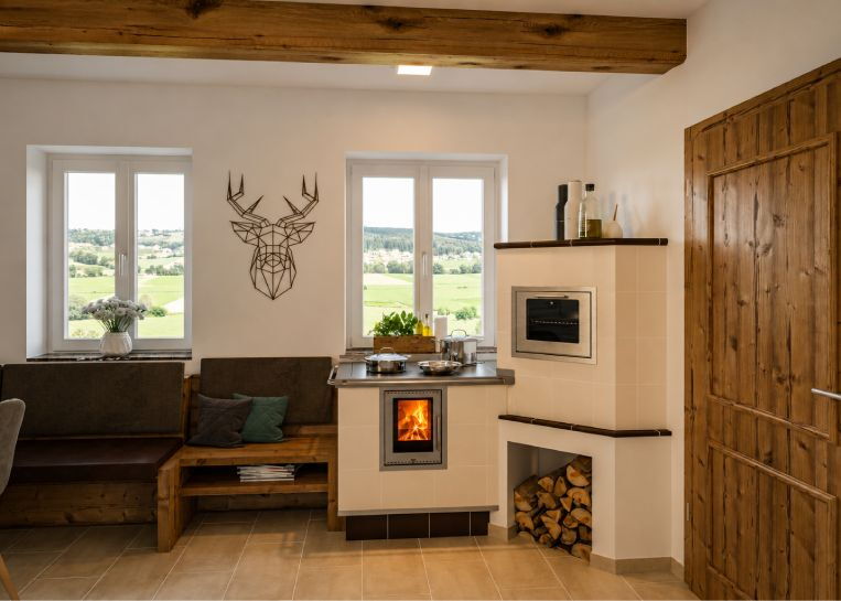 Frontale Ansicht der Herdanlage mit großem Sichtfenster auf das Feuer, Edelstahl-Reling und angrenzender Holz-Sitzbank.