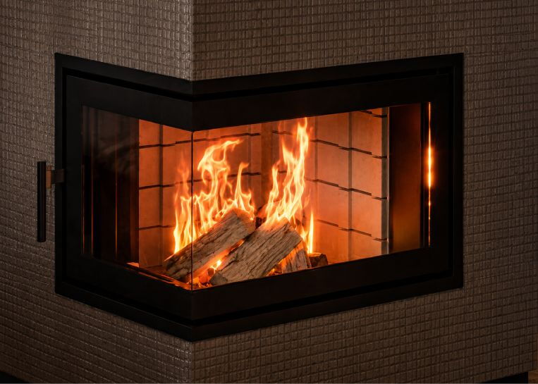 Nahaufnahme der L-förmigen Glasscheibe des Kombiofens, die den Blick auf das lodernde Holzfeuer und die Schamotte-Auskleidung freigibt.