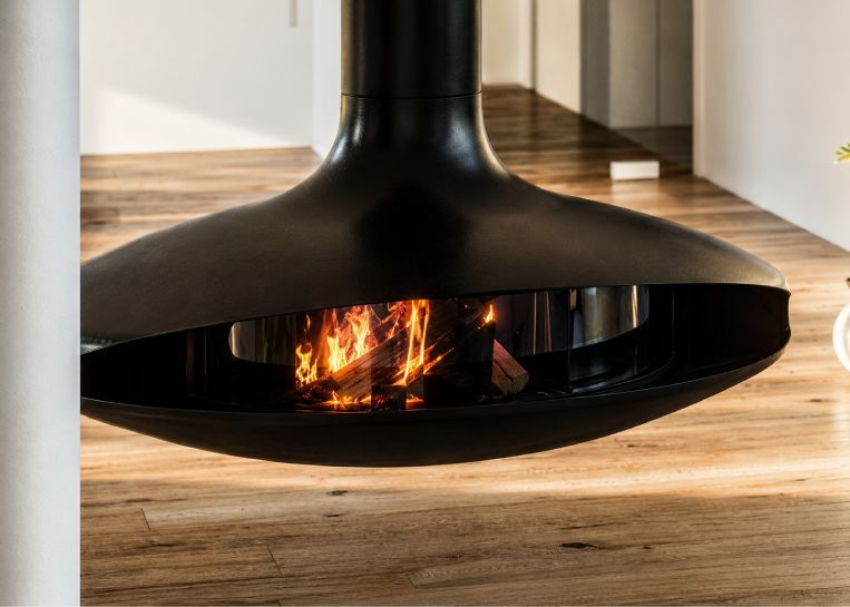 Nahaufnahme des lodernden Holzfeuers in der kreisrunden, durch gebogenes Glas geschlossenen Brennkammer des Focus Kamins.