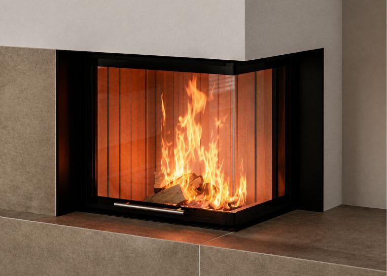 Nahaufnahme des lodernden Holzfeuers hinter der Eck-Sichtscheibe, eingerahmt von einer schützenden, massiven schwarzen Metallblende.
