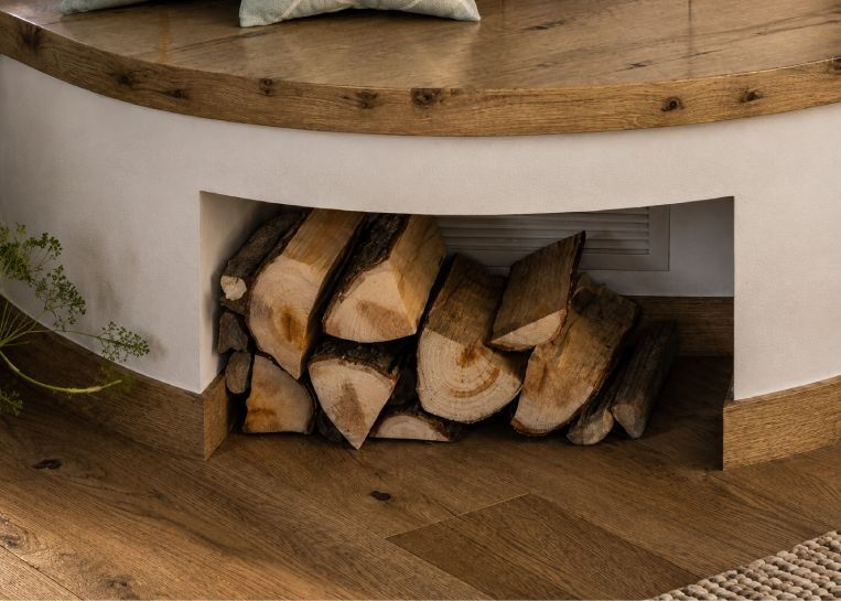 Nahaufnahme des unter der Sitzbank integrierten Holzlagers, das Funktionalität und Ästhetik im Ofendesign verbindet.