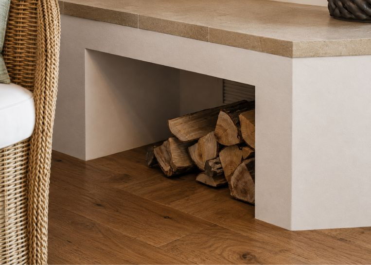 Nahaufnahme der praktischen Holznische unter der Naturstein-Sitzbank, gefüllt mit trockenem Brennholz.