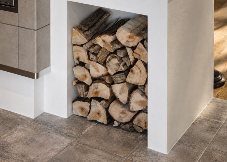 Nahaufnahme des großzügig dimensionierten Holzlagers, das bündig in den grauen Keramikunterbau des Herdes eingelassen ist.
