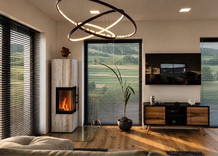 Perspektivische Ansicht des Kaminofens, die das Zusammenspiel von Naturstein, modernem Lichtdesign und dem Blick ins Grüne zeigt.