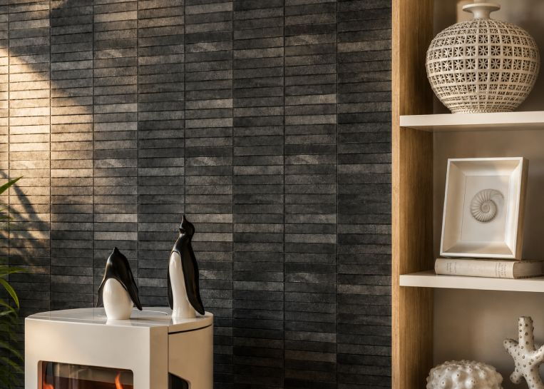 Nahaufnahme der dunklen Riemchen-Wand hinter dem Kaminofen mit zwei dekorativen Pinguin-Figuren auf dem Ofensims.