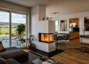 Ein moderner 3-seitiger Panoramakamin Spartherm ARTE U70h mit weißem Ofenkörper als zentrales Designelement im Wohnzimmer.