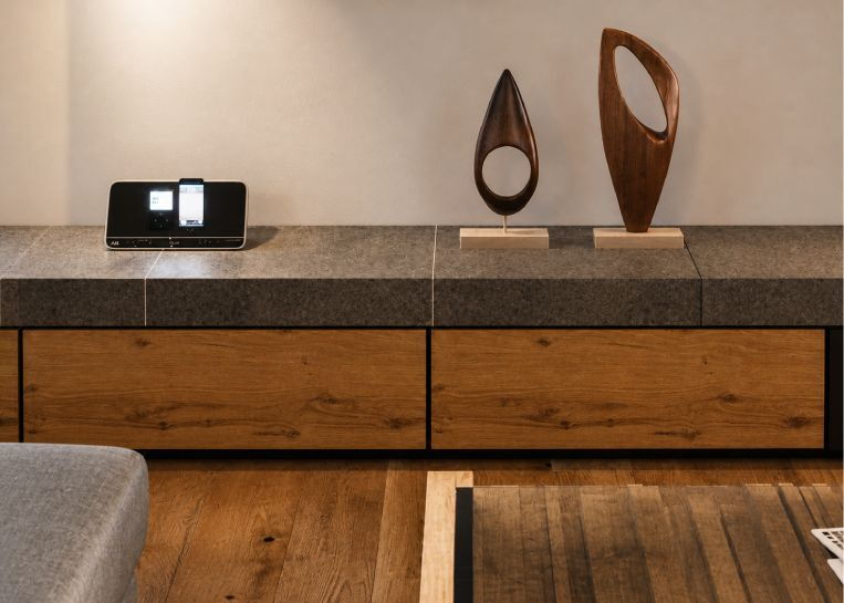 Nahaufnahme der Kaminbankverlängerung mit großformatigen grauen Keramikplatten und edlen Schubladenfronten aus Naturholz.