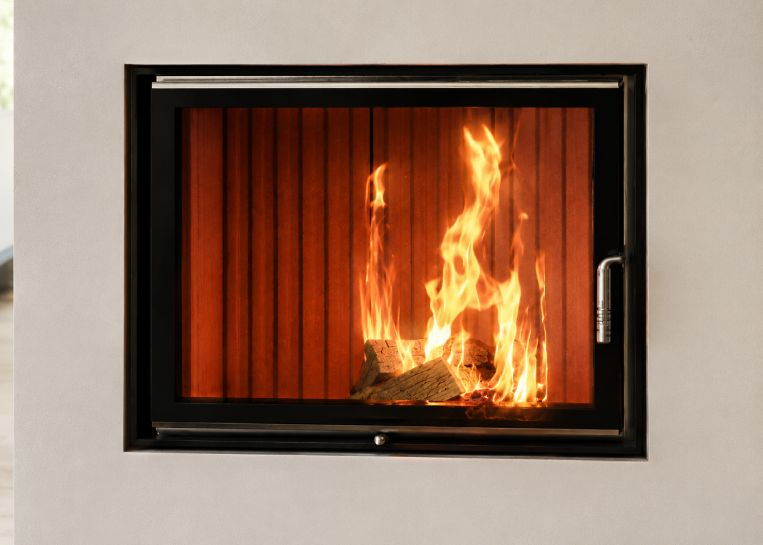 Nahaufnahme des Feuerraums hinter der Brunner Grundofentür mit ihrer charakteristischen, massiven Metallblende.