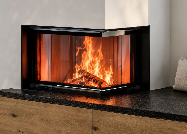 Nahaufnahme der brennenden Eck-Sichtscheibe des Brunner GOT, eingerahmt von einer schwarzen Blende auf einem dunklen Naturstein-Feuertisch.