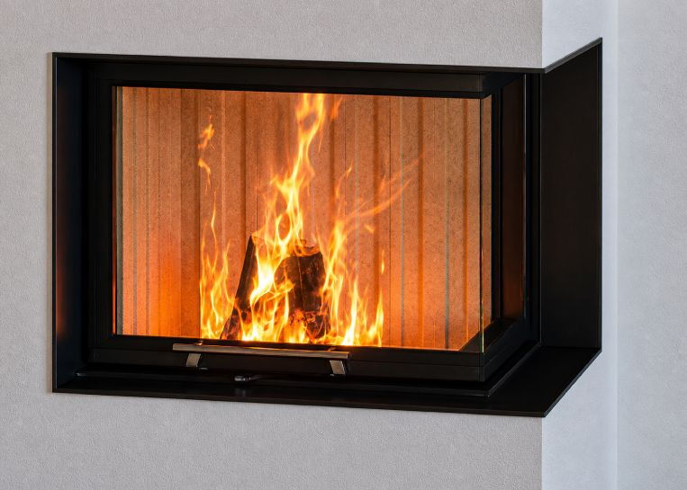 Nahaufnahme des lebendigen Flammenspiels hinter der Ecksichtscheibe, die von einer präzisen schwarzen Metallblende eingerahmt wird.
