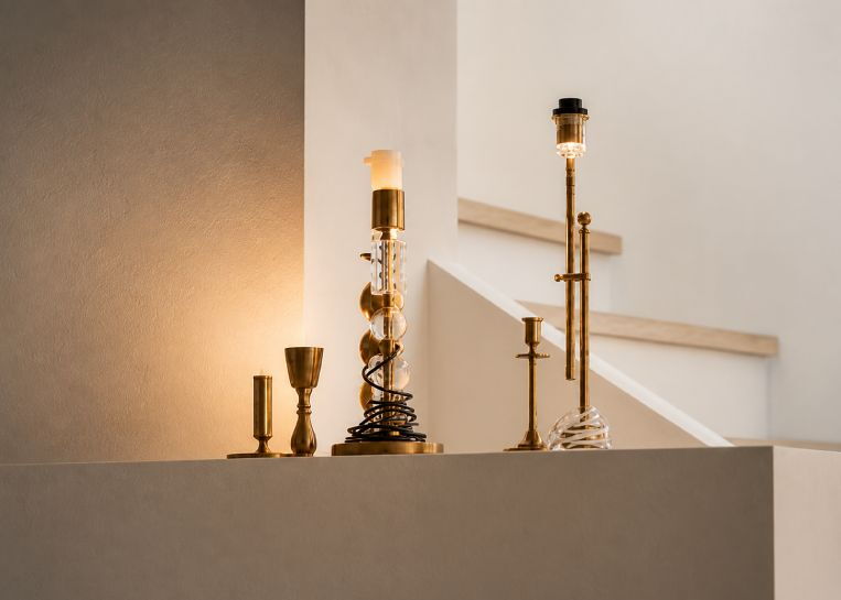 Detaillierte Ansicht von stilvollen, goldenen Kerzenständern auf der weißen Kaminabdeckung vor dem Treppenaufgang.