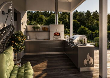 Gesamtansicht einer modernen L-förmigen Outdoor-Küche mit integriertem Pizzaofen, Gasgrill und Spüle auf einer überdachten Terrasse.