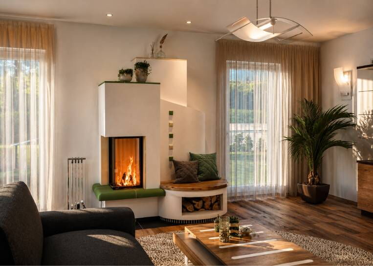 Ein moderner, weißer Eckkamin mit hochgestelltem Spartherm Sichtfenster und einem grünen Feinkeramik-Feuertisch im Wohnzimmer.