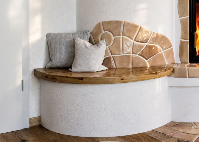 Nahaufnahme der Holz-Sitzbank mit gemütlichen Kissen und der kunstvoll direkt an den Ofen modellierten Handformkeramik.