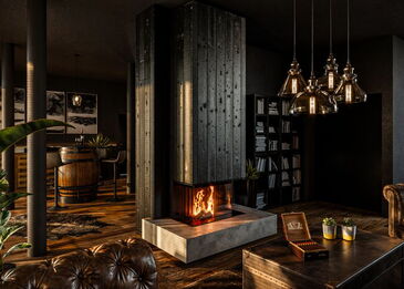 Ein moderner 3-seitiger Panoramakamin Spartherm Lean 3LR-70h, verkleidet mit außergewöhnlichem karbonisiertem Holz und einem Feuertisch in Betonoptik.